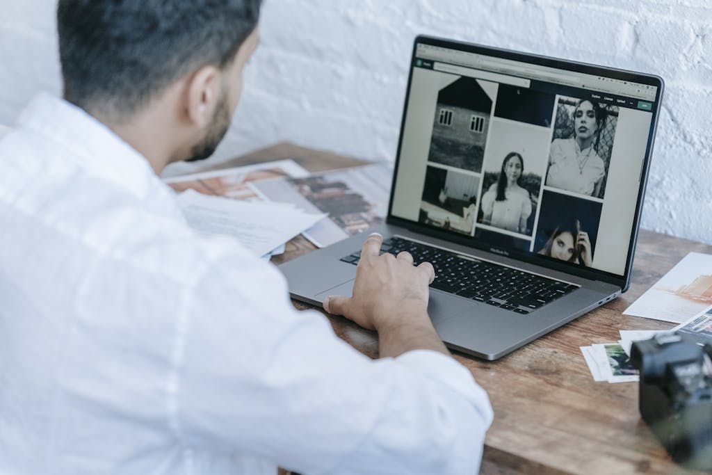 Side view of crop bearded male photographer using laptop while preparing pictures for publishing in modern workplace